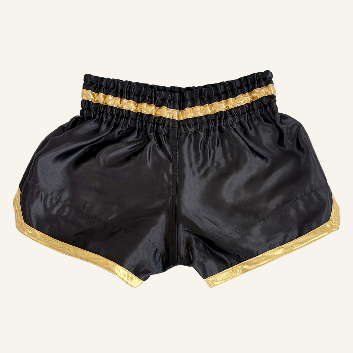 Black satin boxing shorts with shiny gold trim along the sides and waistband, shown flat against a white background.