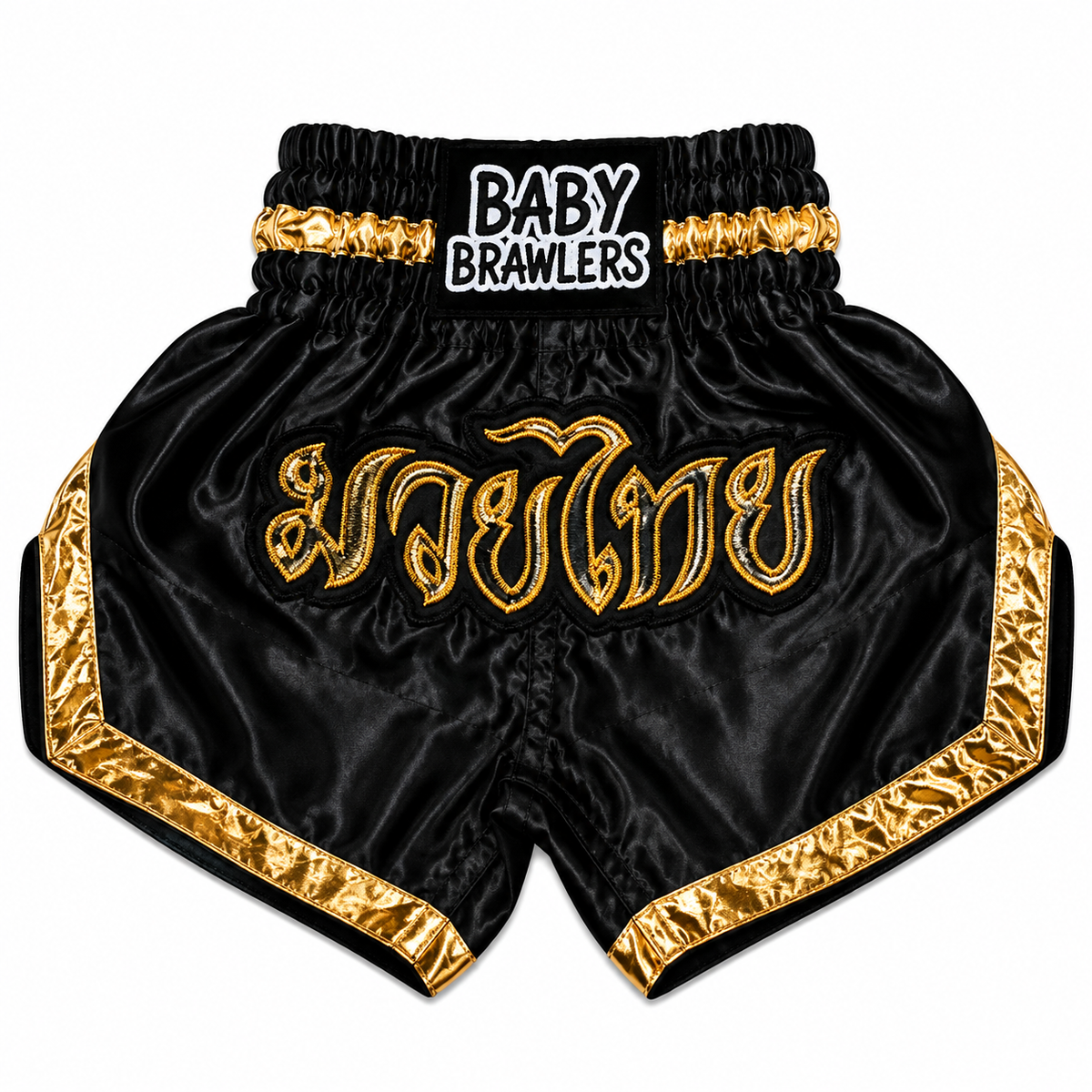 Black satin Muay Thai shorts with gold trim and Thai script embroidery on the front, featuring a black elastic waistband with a 'BABY BRAWLERS' logo patch.