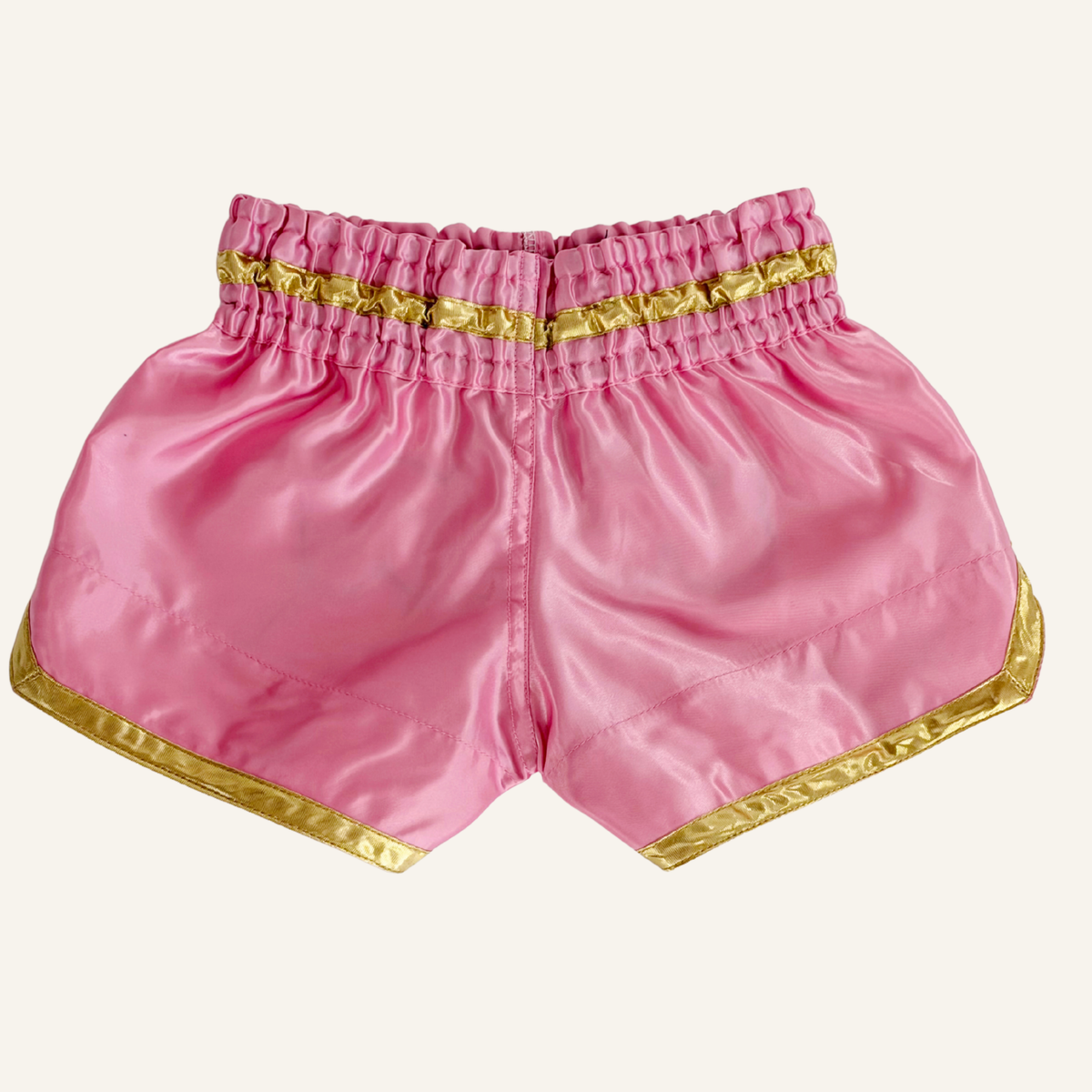 Pink satin Muay Thai shorts with gold metallic trim and an elastic waistband, shown flat on a white background.