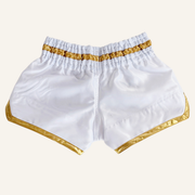 White satin martial arts shorts with shiny gold trim and an elastic waistband, shown flat against a white background.