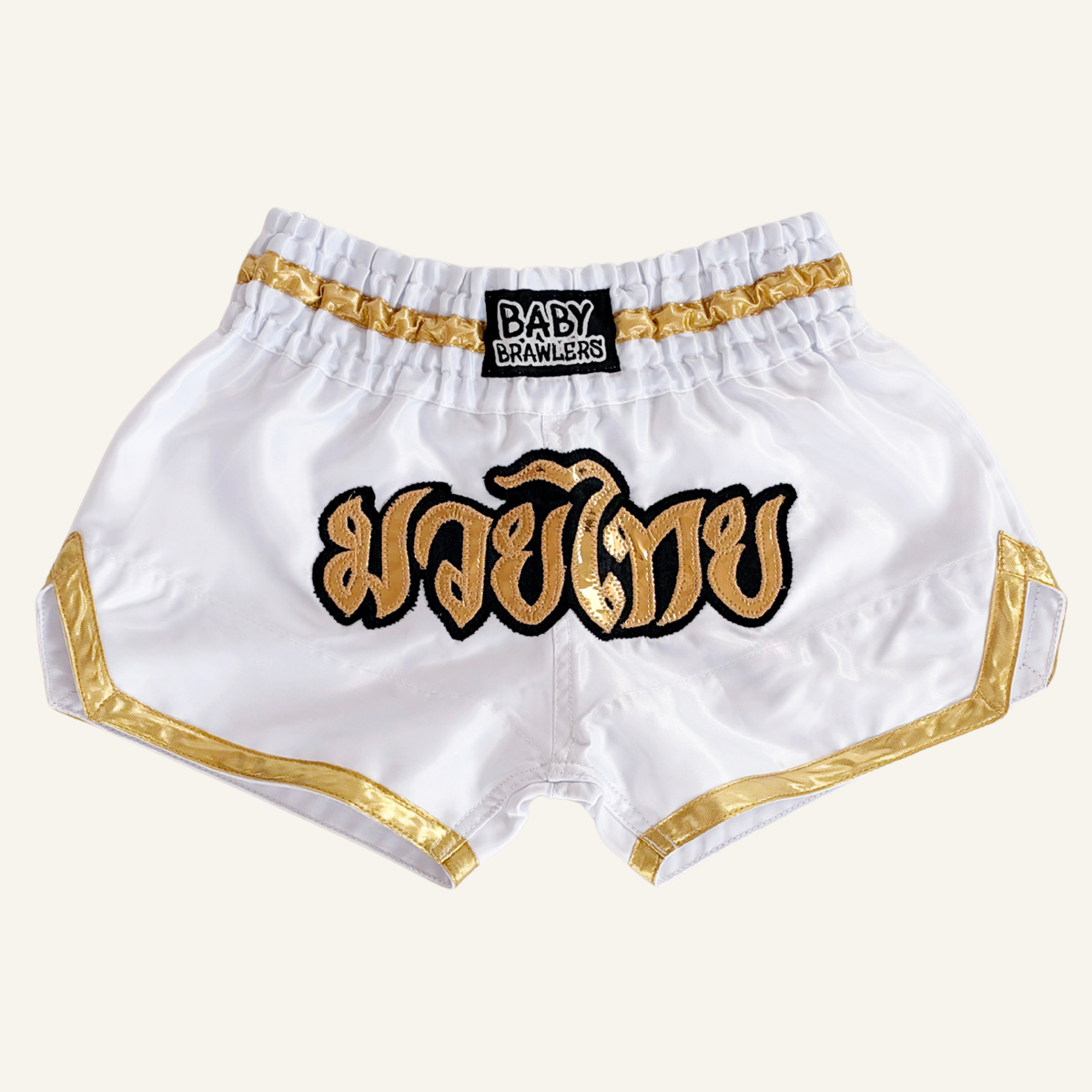 Pink satin Muay Thai shorts with gold and black trim, featuring a large gold Thai script patch on the front and a black waistband patch reading 'BABY BRAWLERS'.