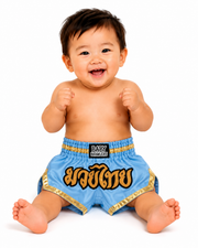 A smiling baby sitting on a white background wearing light blue Muay Thai shorts with gold trim and a black waistband patch that reads 'BABY BRAWLERS'.